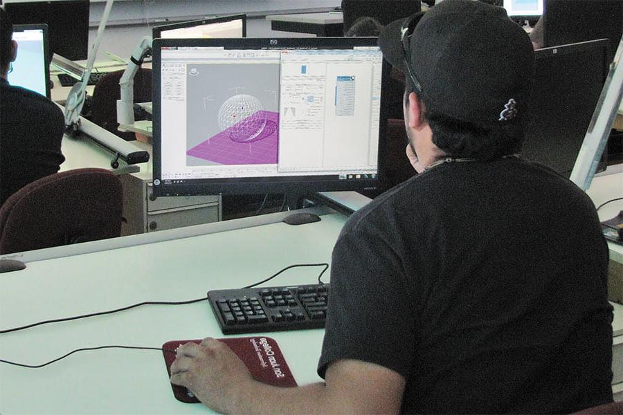 An individual wearing a black baseball hat sits in front of a computer monitor